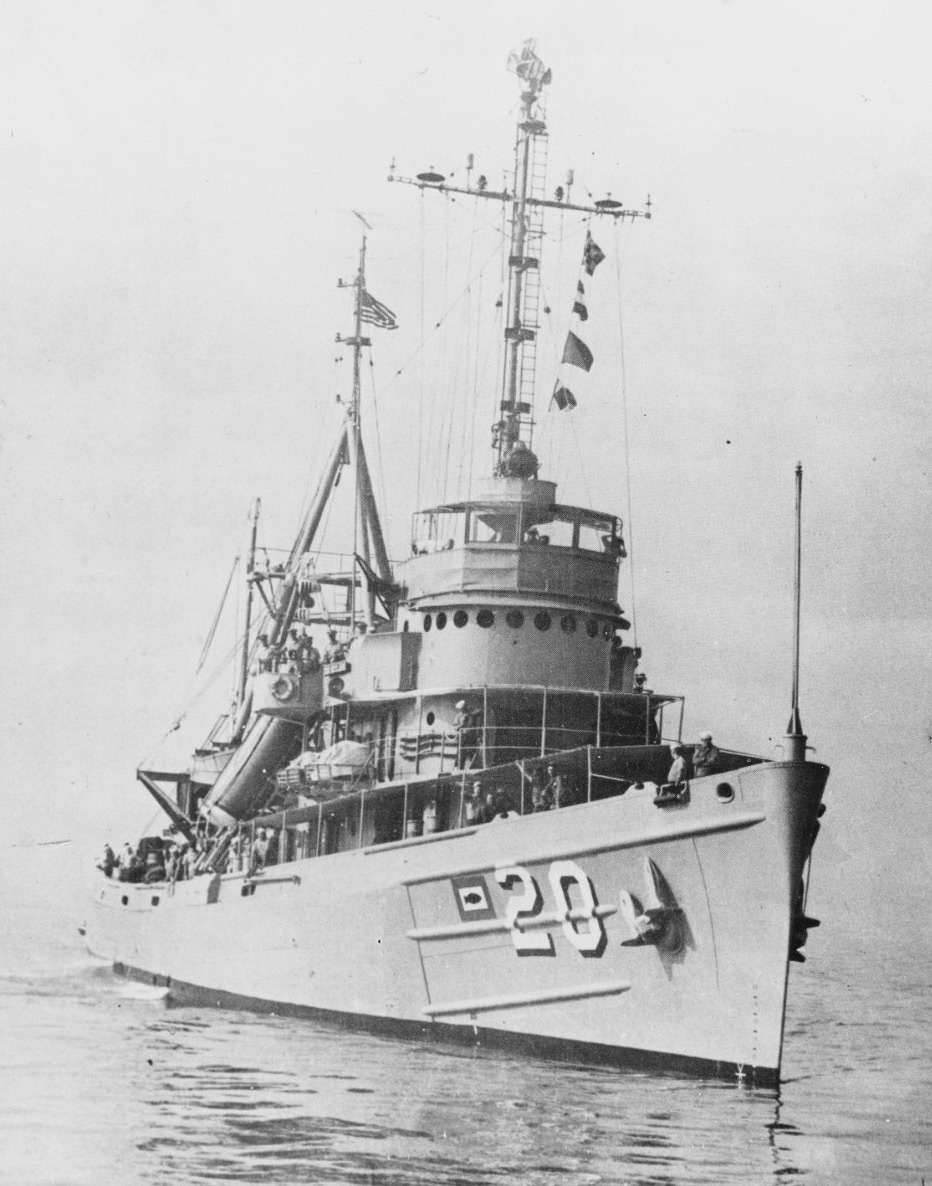 A grey submarine rescue ship with a tall lattice mast and the number 20 on her bow lies at anchor on a calm sea in a coarse halftone print