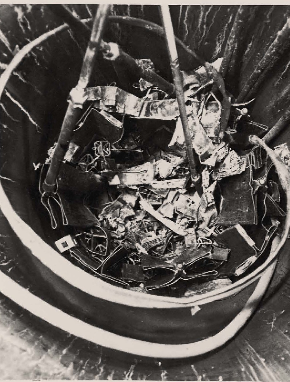 Looking down into a round steel vessel at a tangle of torn, twisted and blackened metal plates with cables hanging into it