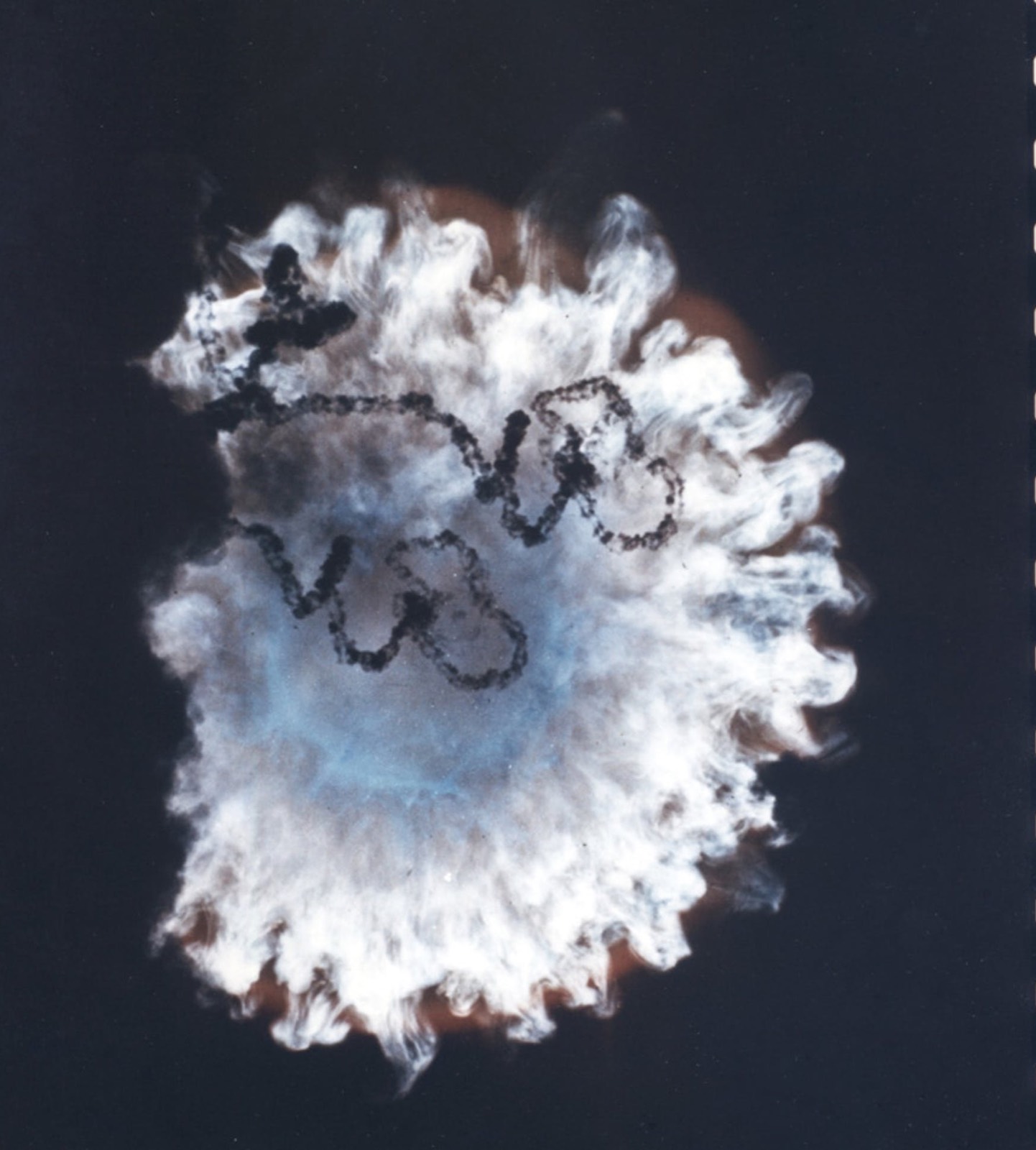 A colour film frame of the Starfish Prime fireball: a white and blue cloud with dark looping trails of debris across it, against black sky