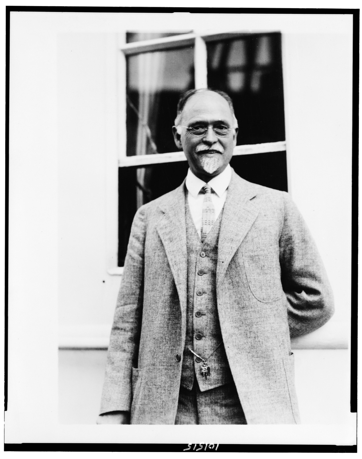 Irving Fisher standing before a window in a tweed three-piece suit, with pince-nez and a white goatee