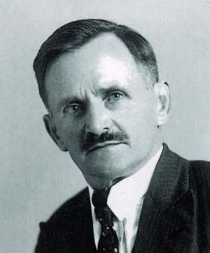 Studio portrait of Michael Unterguggenberger, a man of about fifty with a moustache, in a dark suit and tie